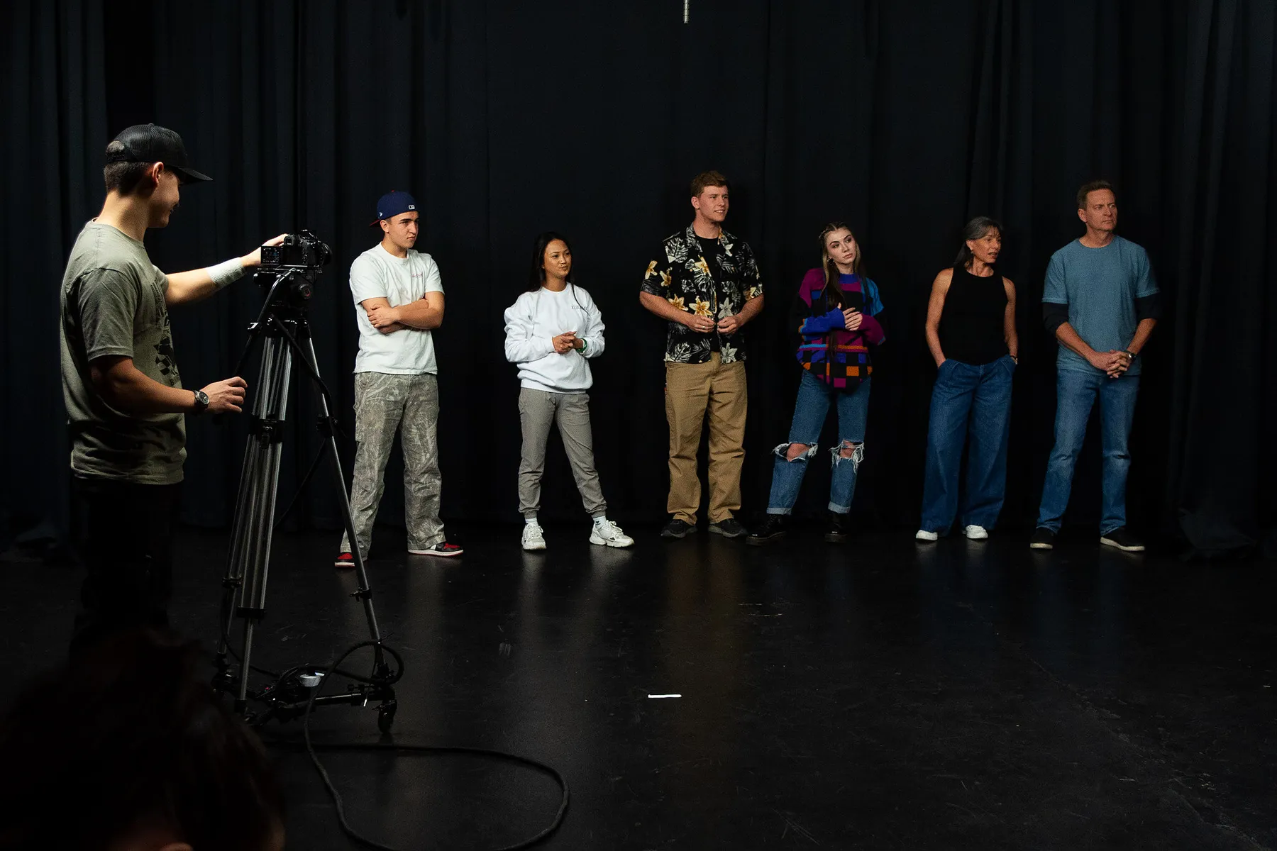 Seven actors on the black stage while the camera is set for callbacks